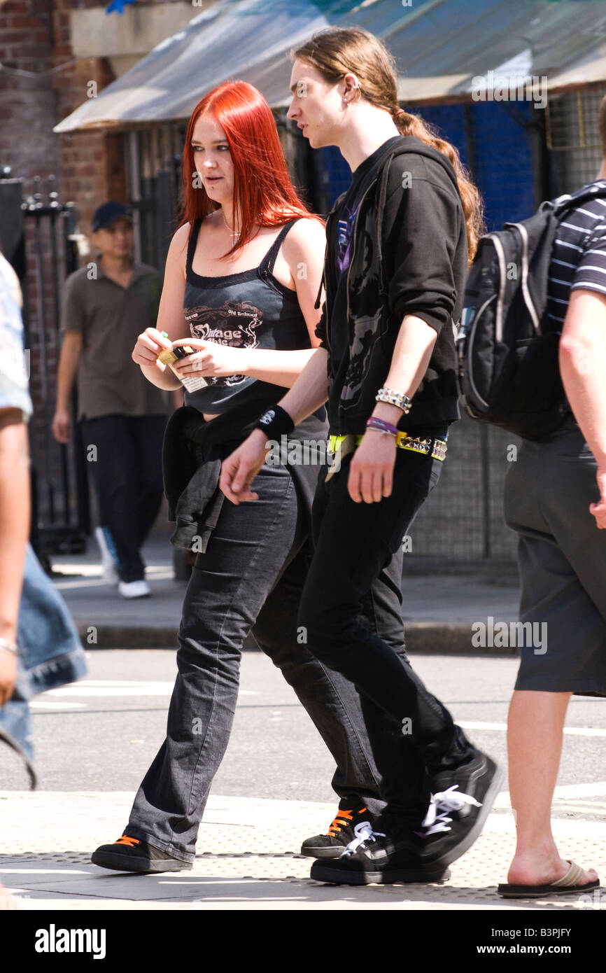 Camden Market Stables , pretty female goth teenage girl with red hair walks with male boy with ponytail dressed in jeans by road Stock Photo