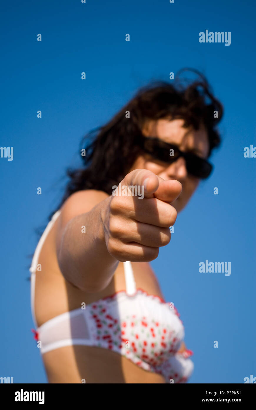 Model Released close up of woman pointing hand with face in background wearing sunglasses and bra Focus on hand Stock Photo