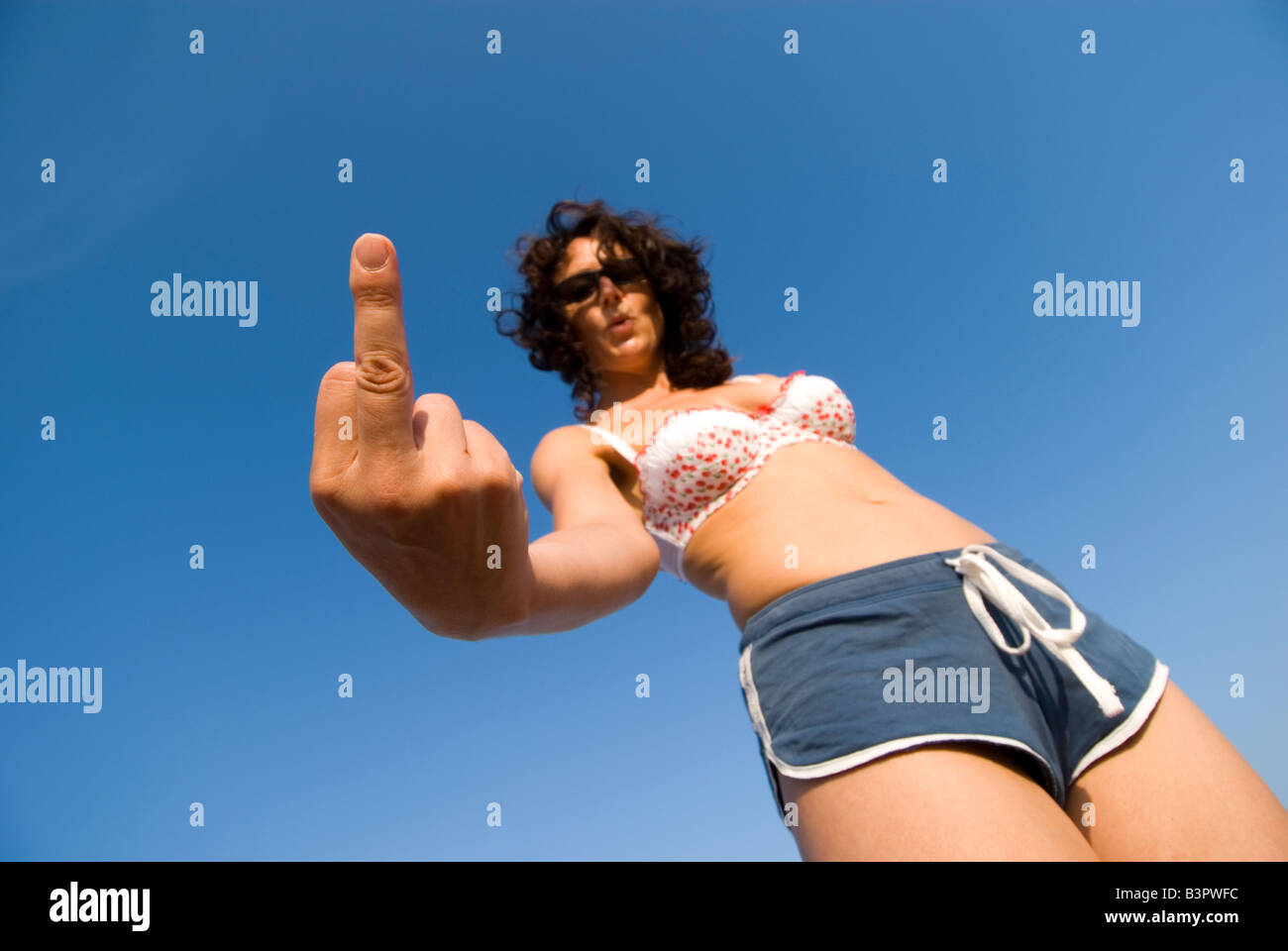 Model Released Female forming an abusive middle finger sign dressed in beachwear Low angle focus on hand Stock Photo