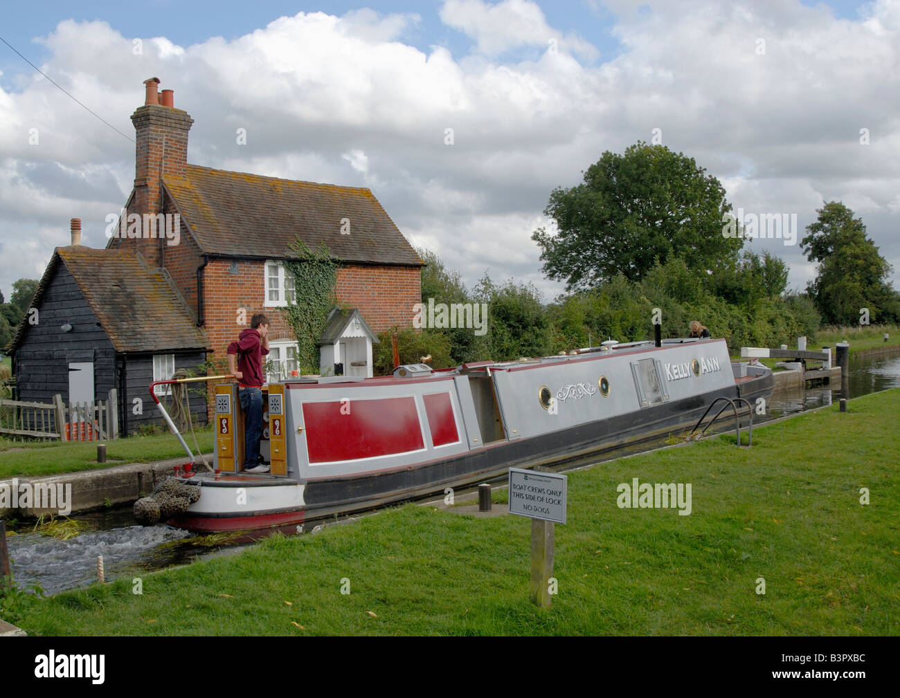 Man on stern of traditional narrowboat passing through Triggs Lock on the River Wey Navigation, near Woking, Surrey, England Stock Photo