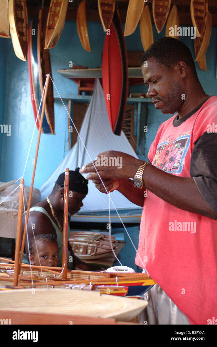 Master model boat builder Jefferson Williams assembles a model boat in the work shop while child watches Stock Photo