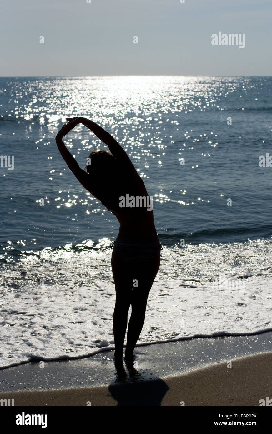 Model Released woman with outstretched arms silhouetted against sea shining from the sun Stock Photo