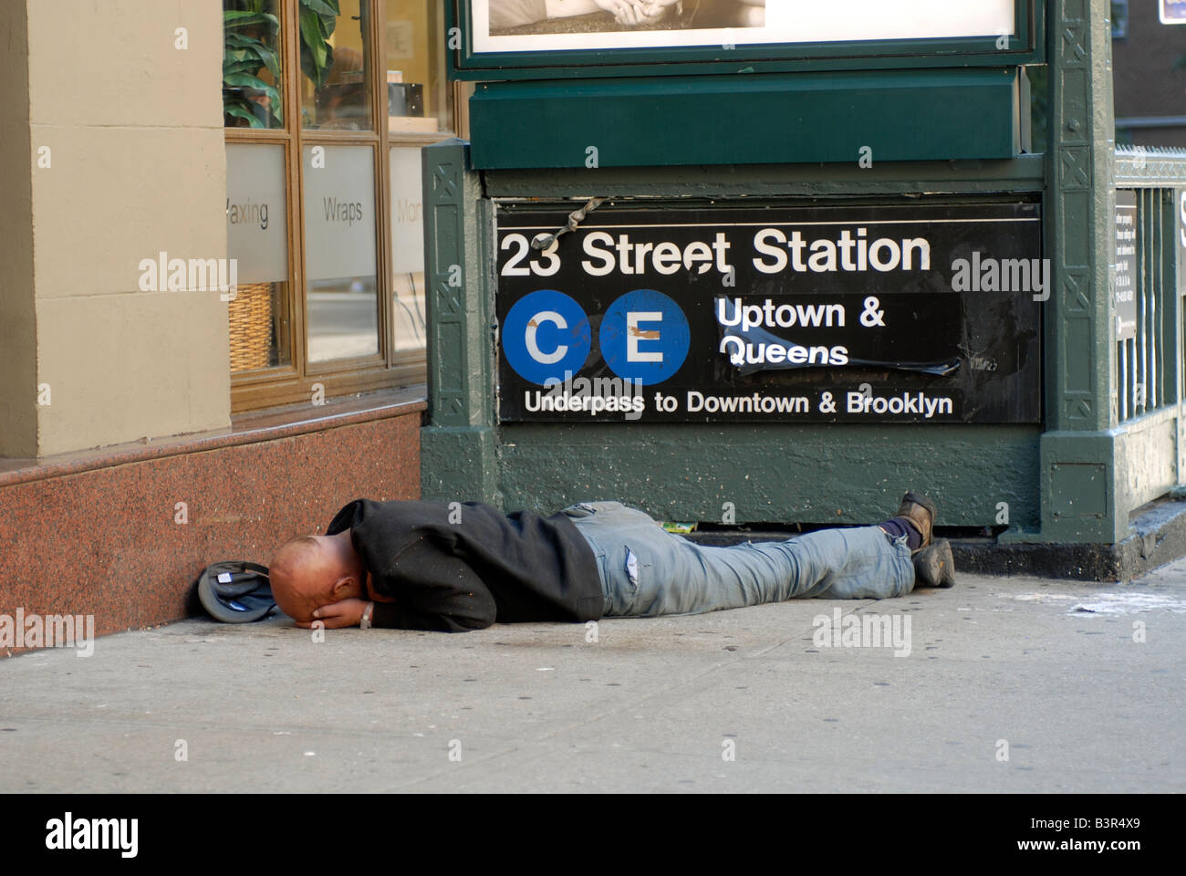 A homeless man sleeps near a subway entrance in the New York neighborhood of Chelsea Stock Photo