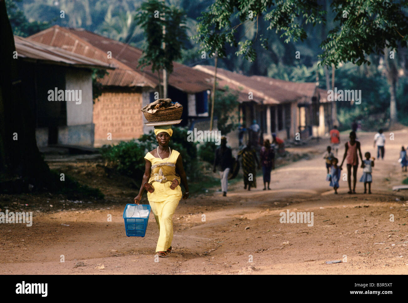 SIERRA LEONE', WOMAN, CARRYING ITEMS IN A BASKET ON HER HEAD, WALKING IN RURAL STREET SCENE, BO, JULY 1992 Stock Photo