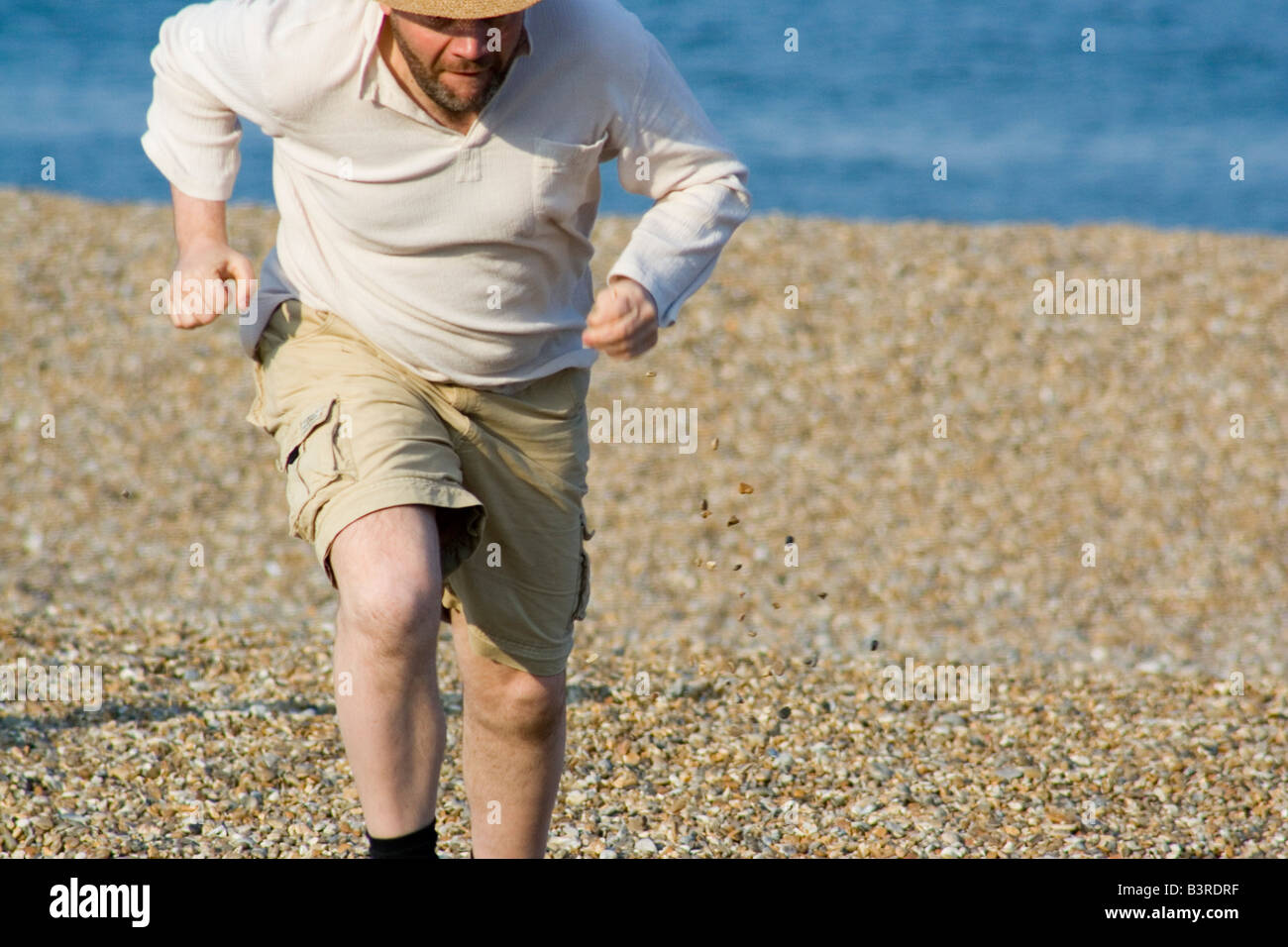 Bearded man in shorts running on Aldeburgh's pebbley beach Stock Photo