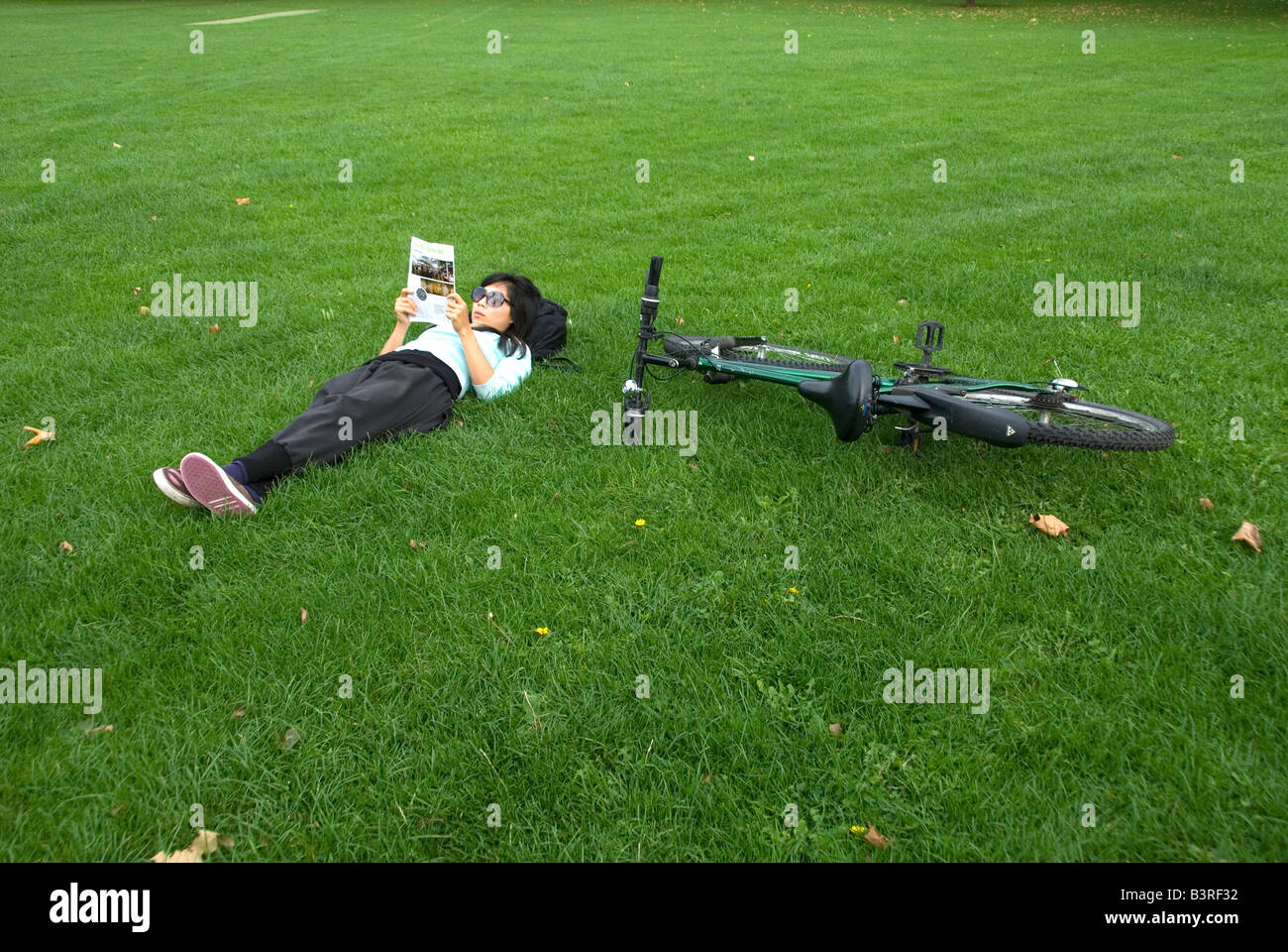 Young woman reading on London Fields next to her bicycle Stock Photo