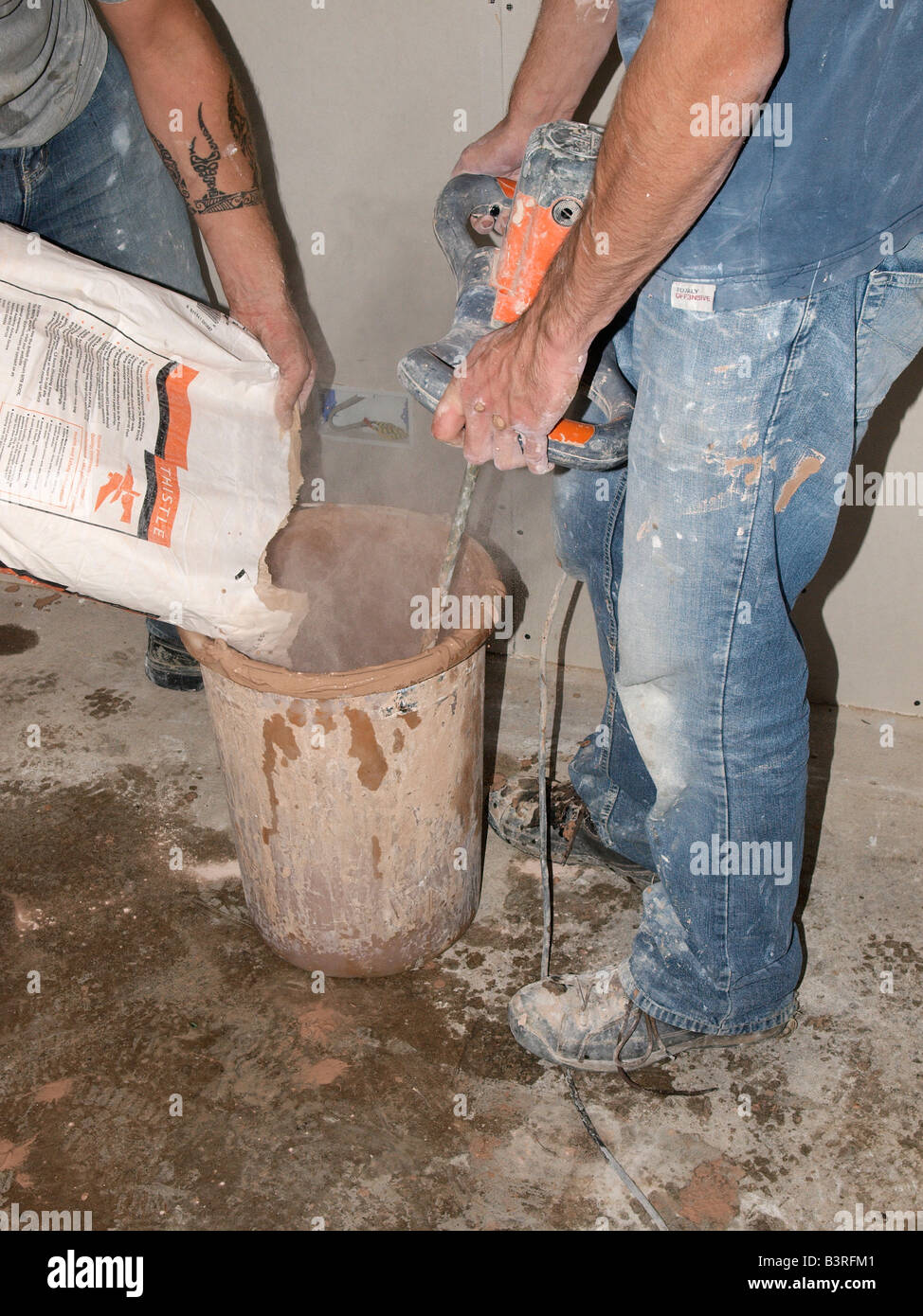 TWO PLASTERERS MIXING DRY PLASTER WITH WATER USING DRILL WITH PADDLE