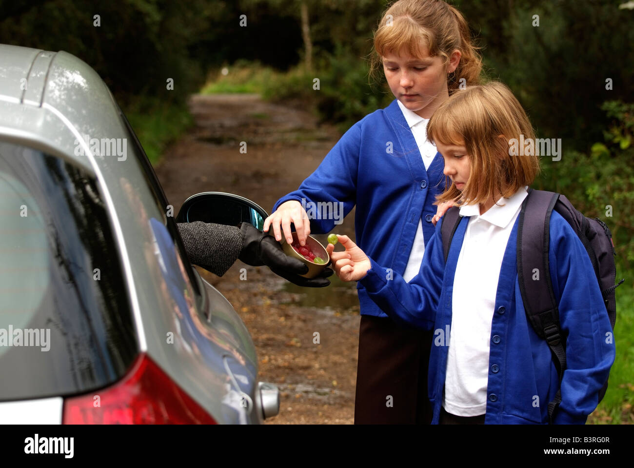 Young girls alone on a country lane taking sweets from a stranger driving a car Never take sweets from a stranger Stock Photo