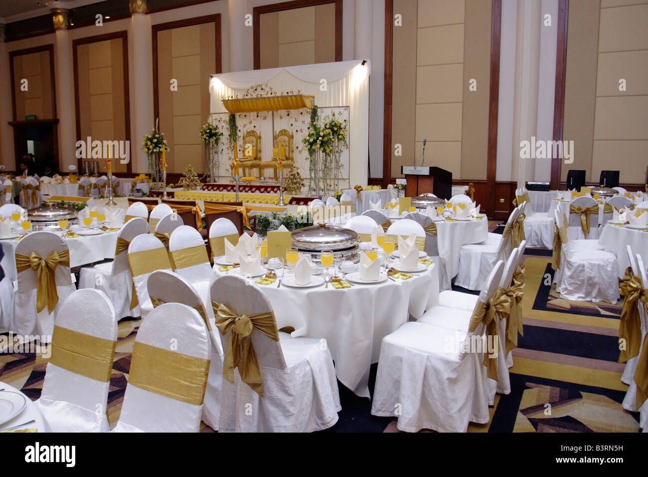 Dining tables for Malay wedding in a hotel. On the background is the dais for the wedding. Stock Photo