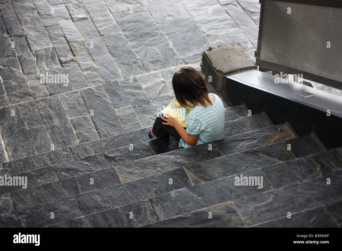 Four year old girl sitting on the stairs reading a map at an aquarium. Stock Photo
