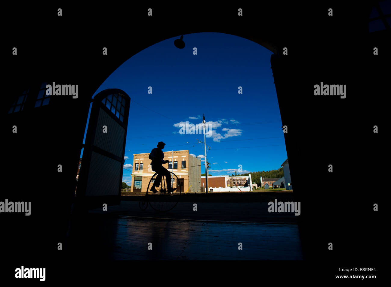 Silhouette of man riding old fashioned bicycle down small town street Stock Photo