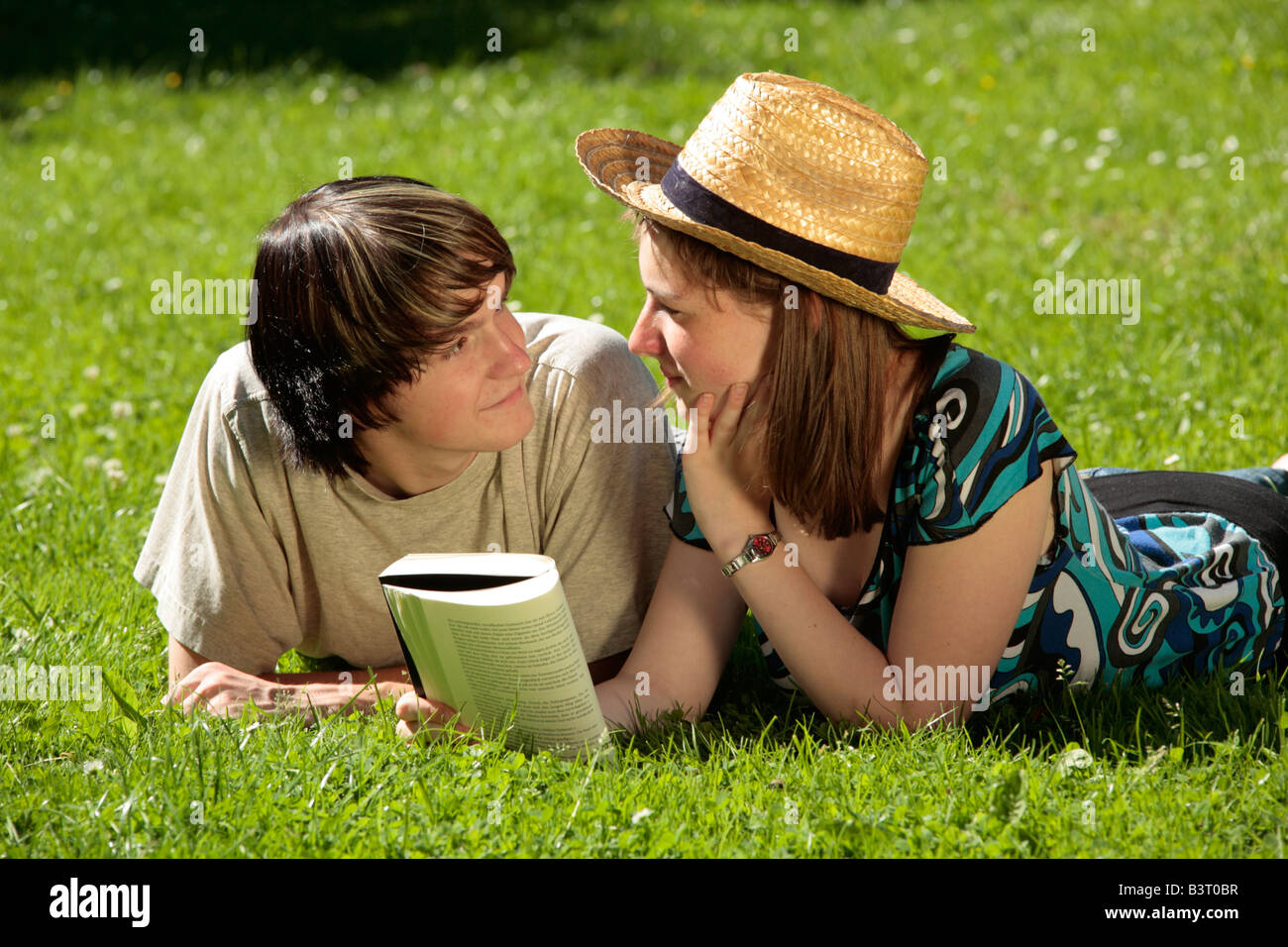 teenage girl and boy lying on a lawn with a book looking at each other ...