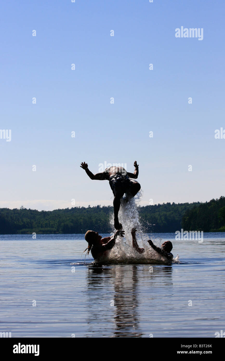 Deer Lake in Michigan USA Three boys brothers men Caucasian having fun playing in water jumping to water jump vertical hi-res Stock Photo