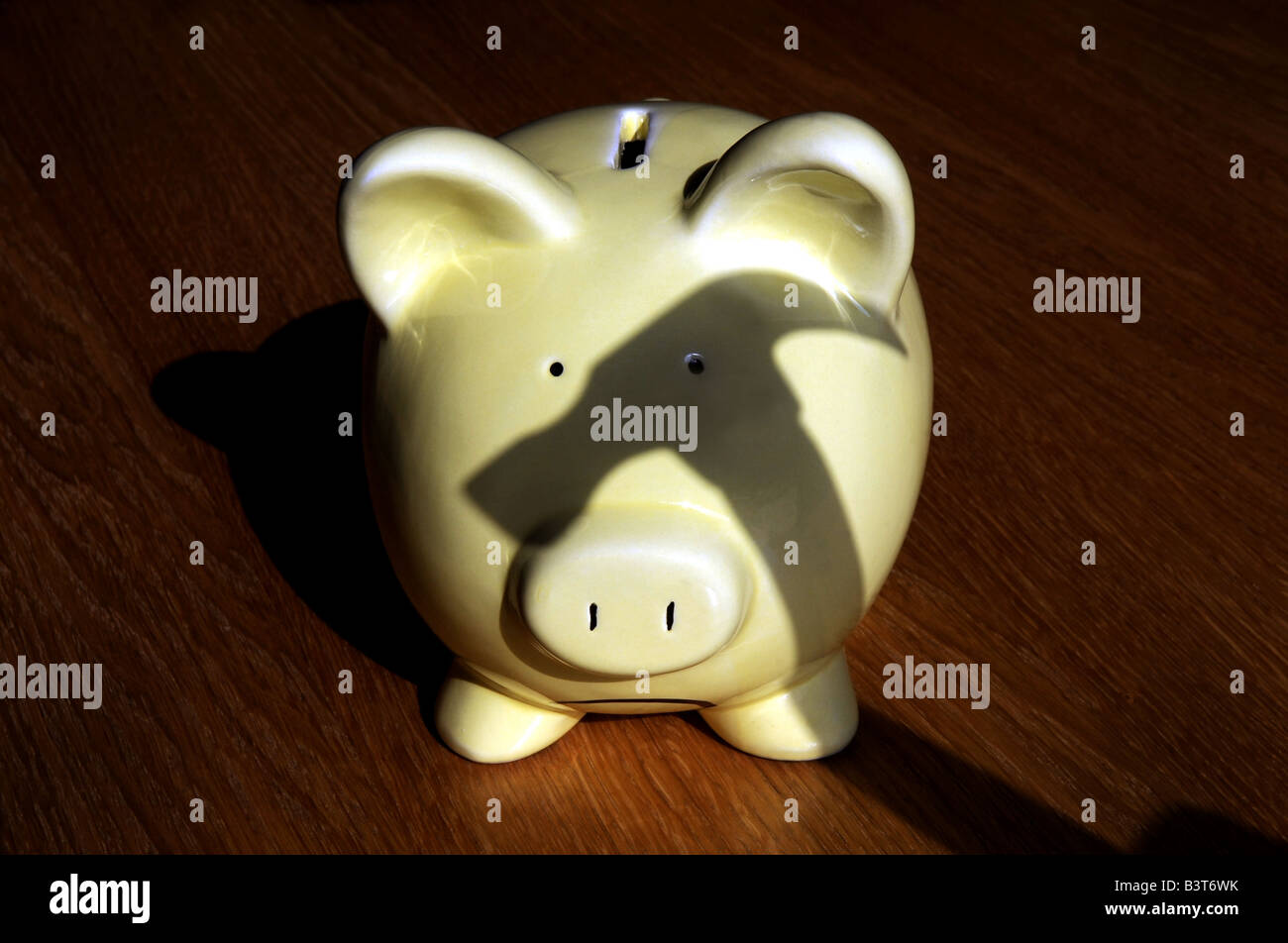 GLUM LOOKING PIGGY BANK WITH SHADOW OF A HAMMER LOOMING OVER IT READY TO SMASH IT. RE THE ECONOMY INCOMES WAGES MORTGAGES UK Stock Photo