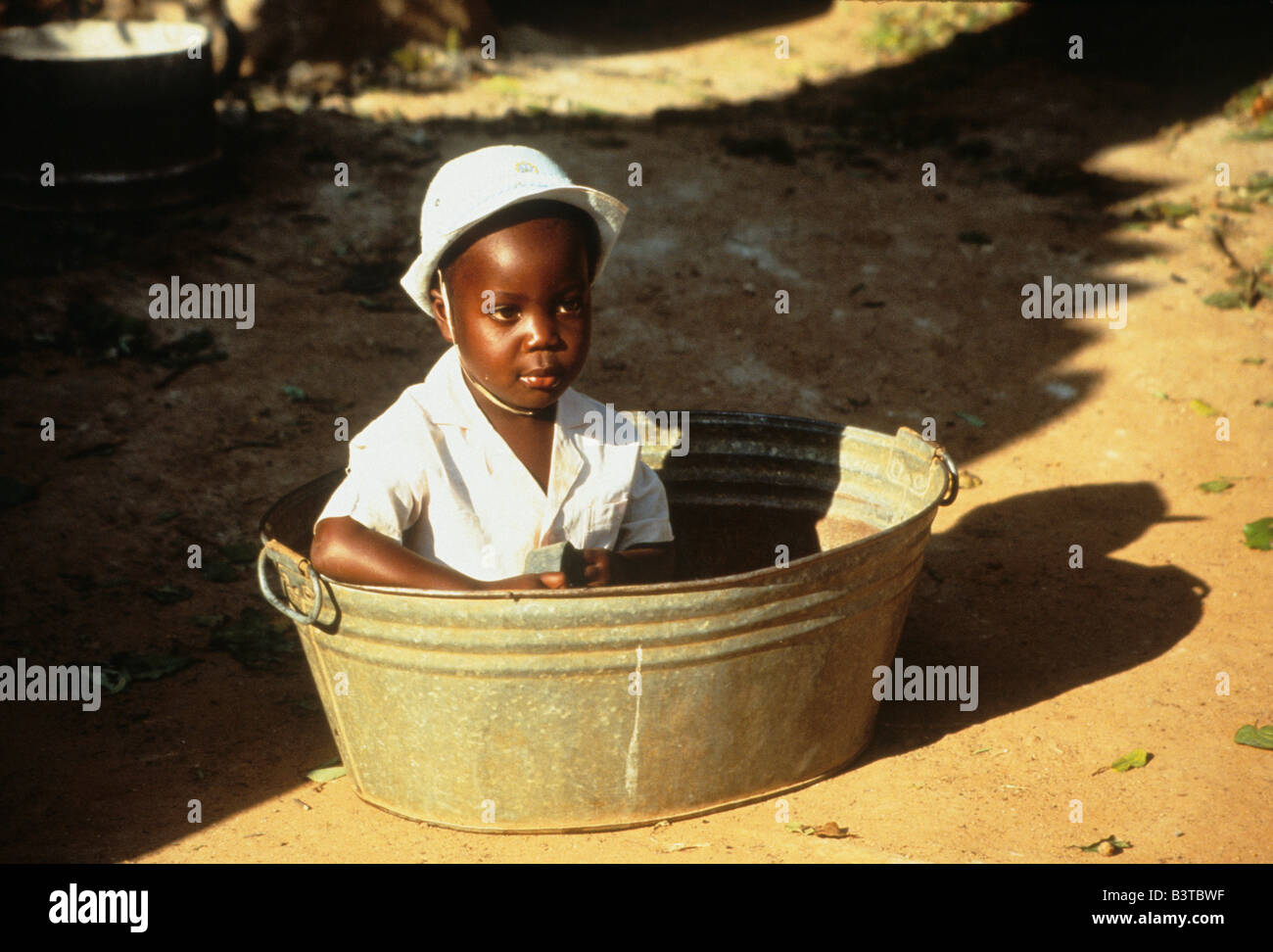 Africa, Zimbabwe. African child sits in tub on private ranch. Stock Photo