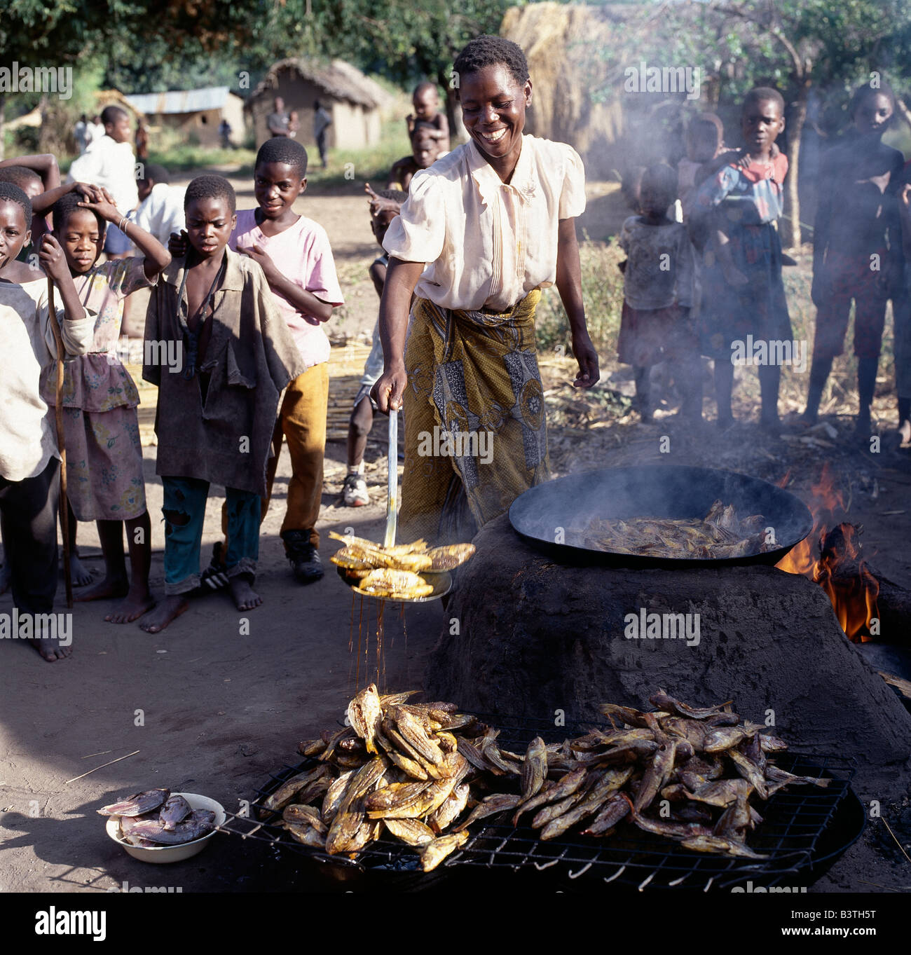 Tanzania, A woman deep-fries small tilapia fish caught in Lake Rukwa, Southwest Tanzania, before sending them to market in Mbeya, which is the commercial centre of the fertile Southern Highlands region. Lake Rukwa is a long, narrow lake lying in a basin of inland drainage southeast of Lake Tanganyika; it forms part of the Western Rift. The lake is very shallow (maximum depth not much more than twenty feet)) and mildly alkaline. Any change in its water level causes great fluctuations of its size. Stock Photo