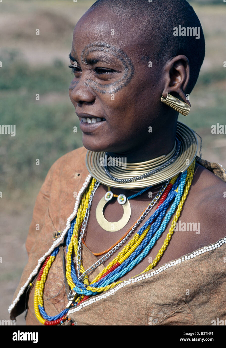 Tanzania, Arusha, Lake Eyasi. A Datoga woman in traditional attire, which includes beautifully tanned and decorated leather dresses and coiled brass necklaces and ear ornaments. Yellow and light blue are the preferred colours of the beads they wear. Extensive scarification of the face with raised circular patterns is not uncommon among women and girls.The Datoga (known to their Maasai neighbours as the Mang'ati and to the Iraqw as Babaraig) live in northern Tanzania and are primarily pastoralists Stock Photo