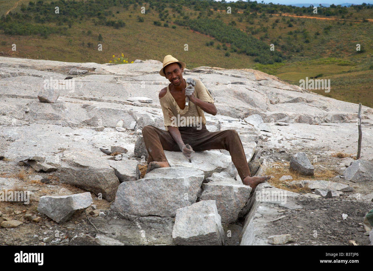 Malagasy happily chiselling granite blocks out of the rock Madagasse sitzt fröhlich auf einem Berg und meißelt Granitsteine Stock Photo