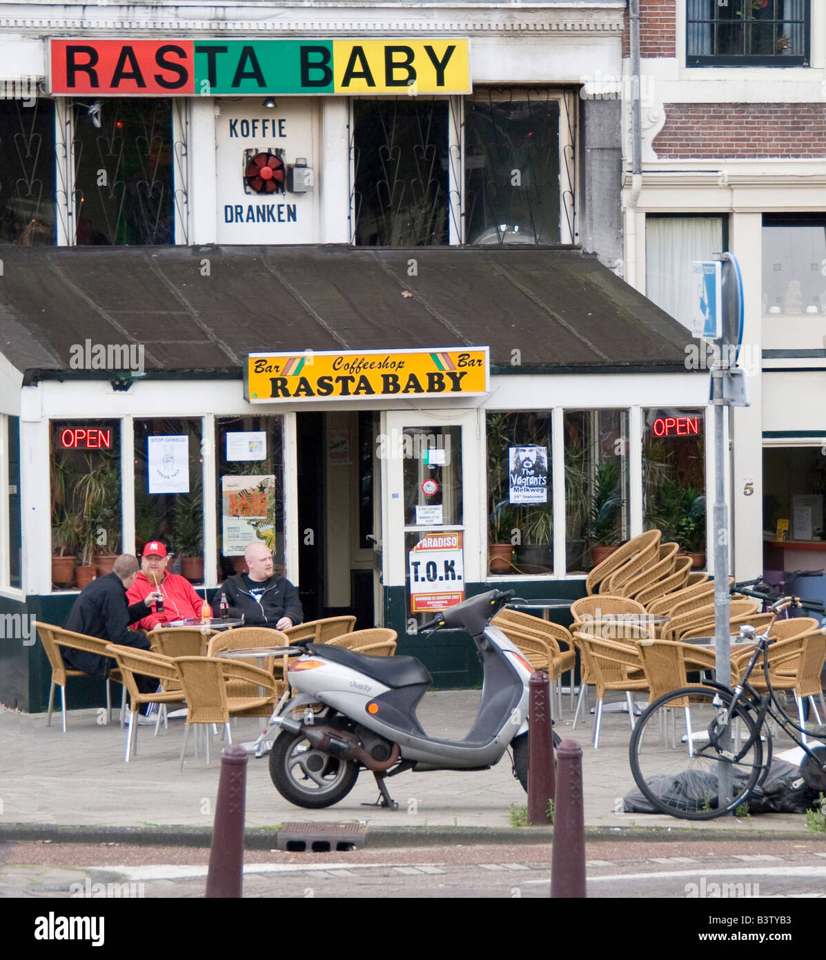 People sitting outside the Rasta Baby coffeeshop with a motorbike and bike parked nearby Stock Photo