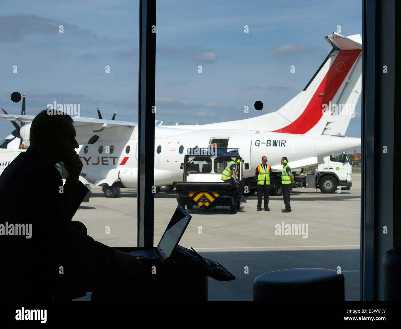 Man using laptop computer at London City Airport with Dornier 328 airplane in the background United Kingdom Stock Photo