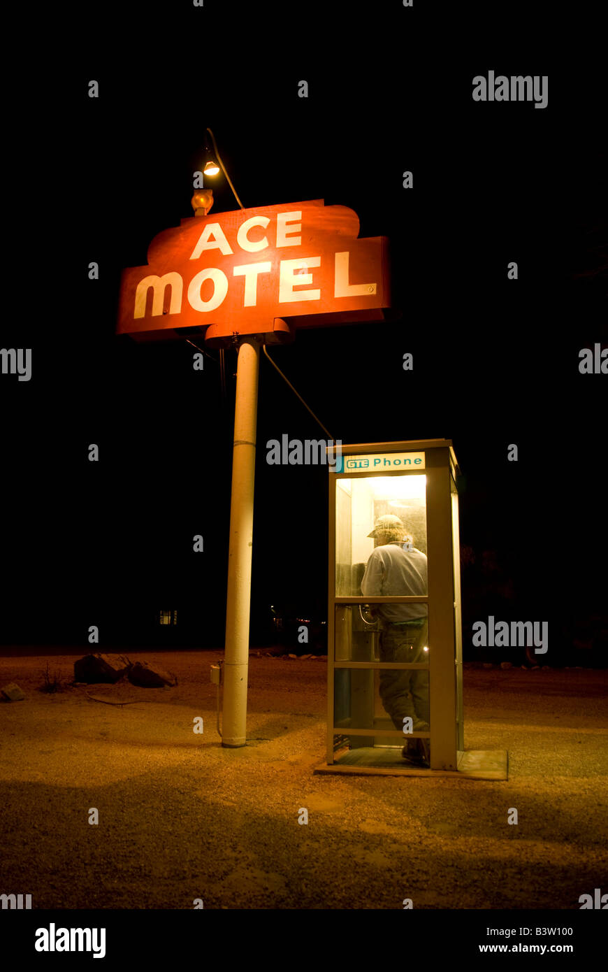 A man making a phone call in a phone booth at night next to a Motel Sign that reads 'Ace Motel'. Stock Photo