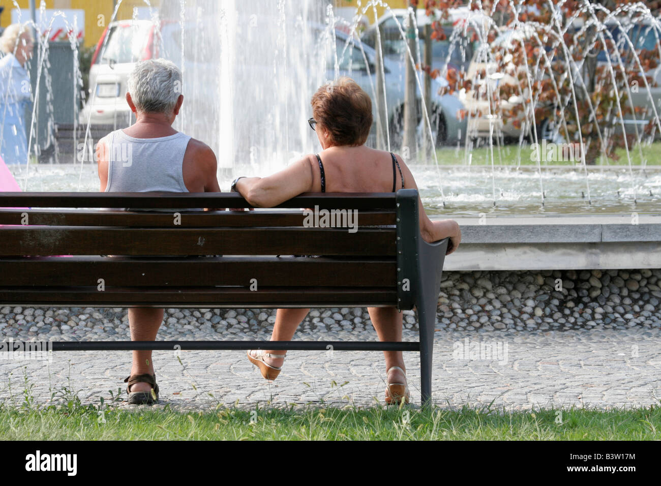 Elderly couple relaxing on a bench by a fountain in a town square Stock Photo