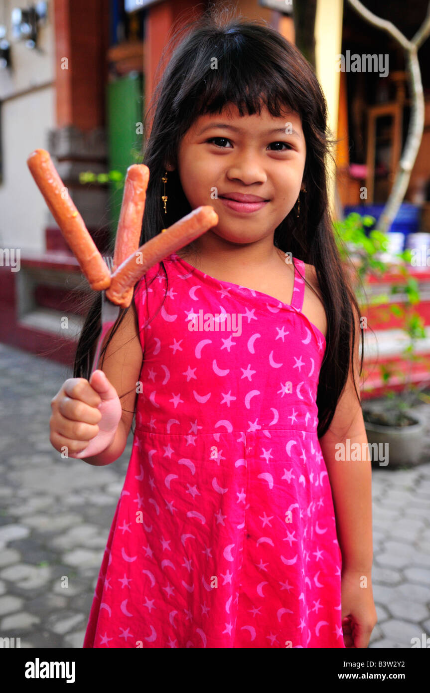 happy and funny young girl with three sausages on a skewer, hot dog without the roll, ubud , island of bali , indonesia Stock Photo
