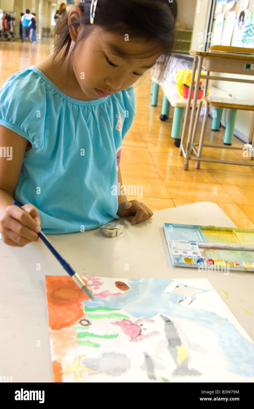 Female Japanese elementary school student painting a picture using delicate brush strokes to paint a picture of sea ocean life Stock Photo