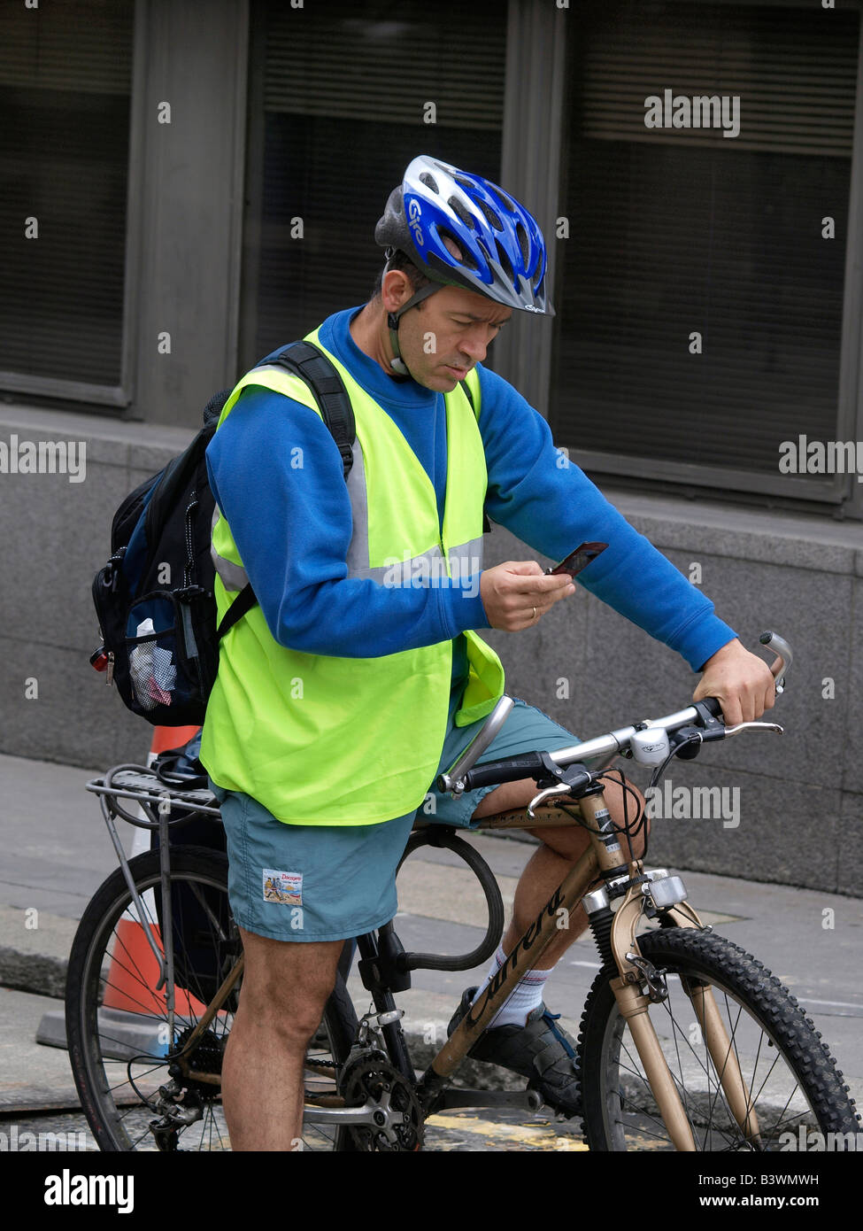 Bicycle courier reading text message on his mobile phone London city United Kingdom Stock Photo