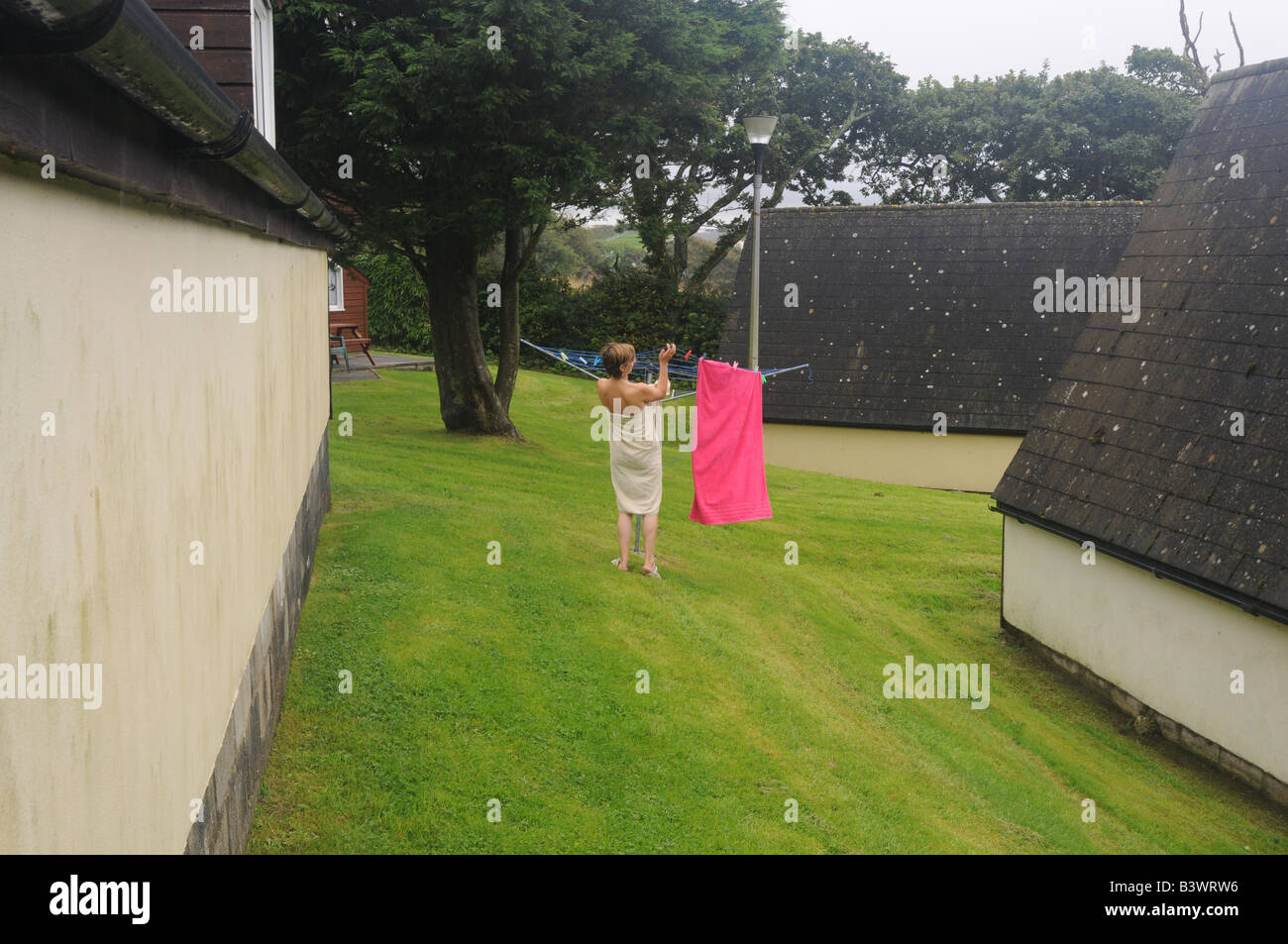 A woman in a towel hangs out damp clothes on a damp holiday outside a