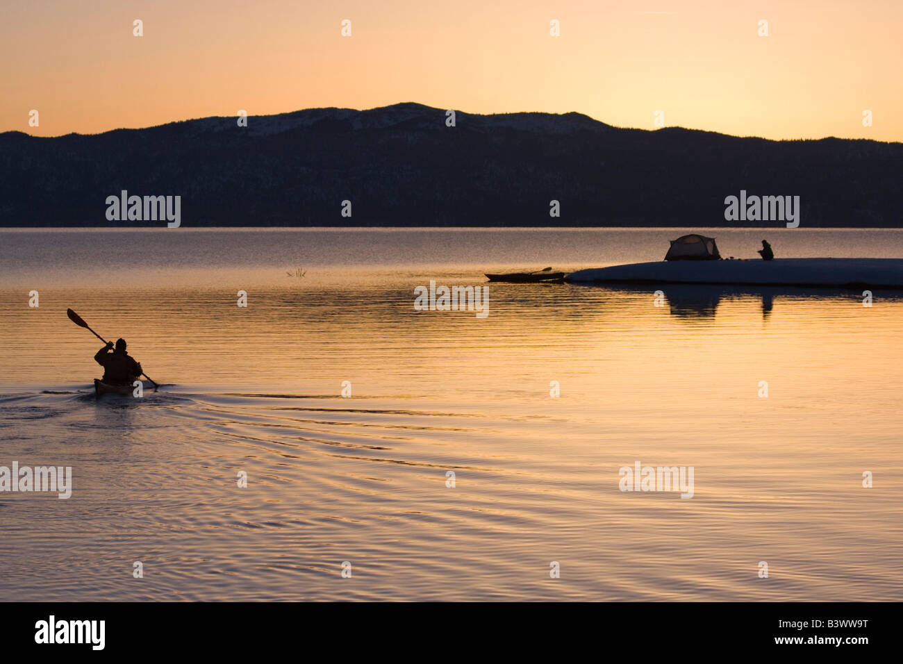 Silhouette of a man kayaking in a lake with a woman near a tent in the background, Lake Tahoe, California, USA Stock Photo