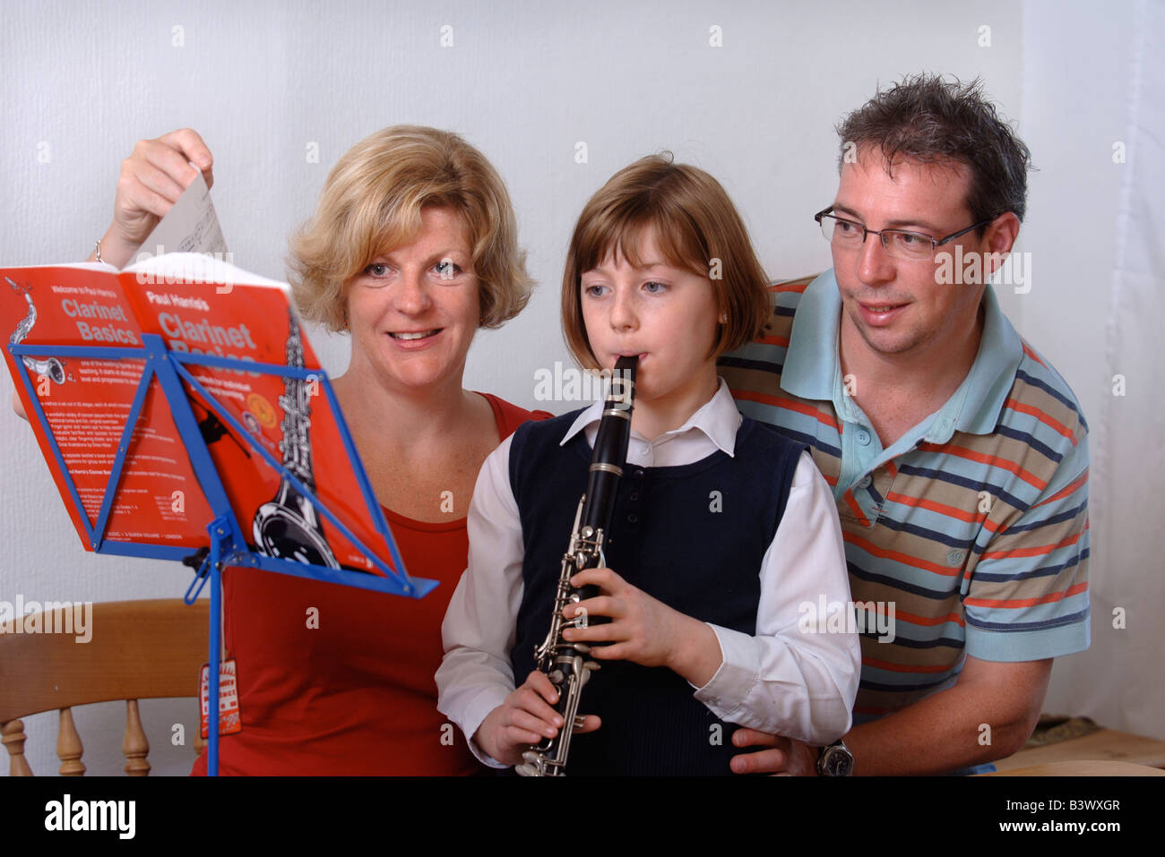 A YOUNG SCHOOLGIRL PRACTICES THE CLARINET HELPED BY HER PARENTS UK Stock Photo