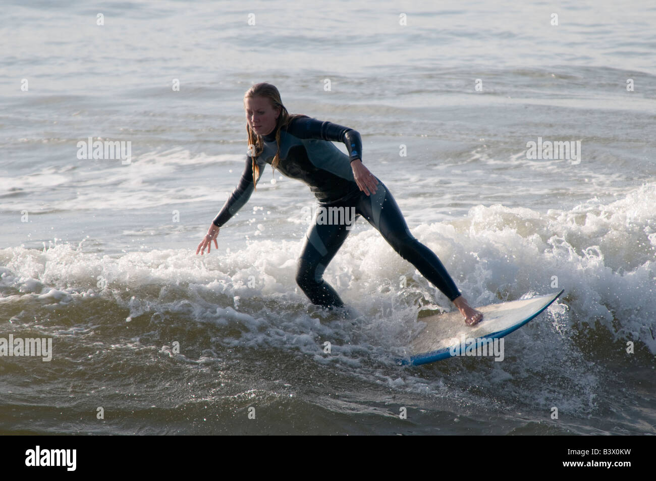 Young blonde teenage girl wearing wetsuit on surfboard surfing on the waves off Aberystwyth Wales UK, summer afternoon Stock Photo