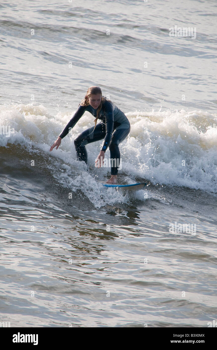 Young blonde teenage girl wearing wetsuit on surfboard surfing on the waves off Aberystwyth Wales UK, summer afternoon Stock Photo