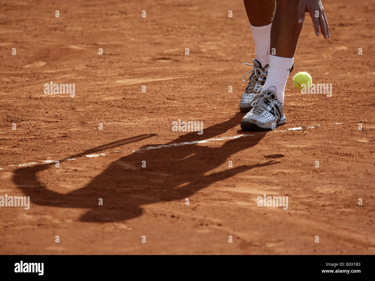Shadow of a tennis player bouncing the ball before the service on a claycourt Stock Photo