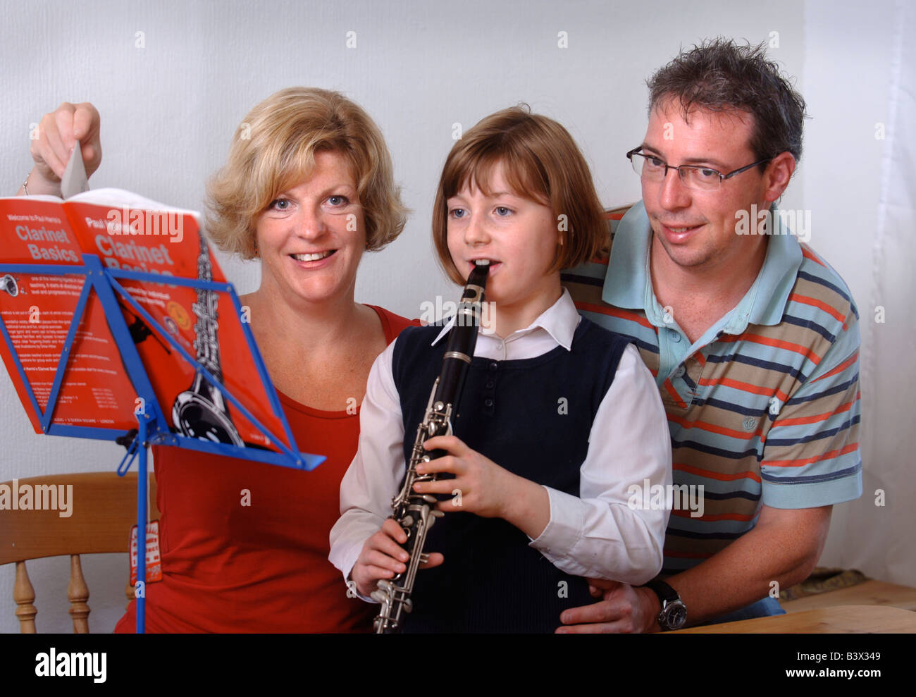 A YOUNG SCHOOLGIRL PRACTICES THE CLARINET HELPED BY HER PARENTS UK Stock Photo