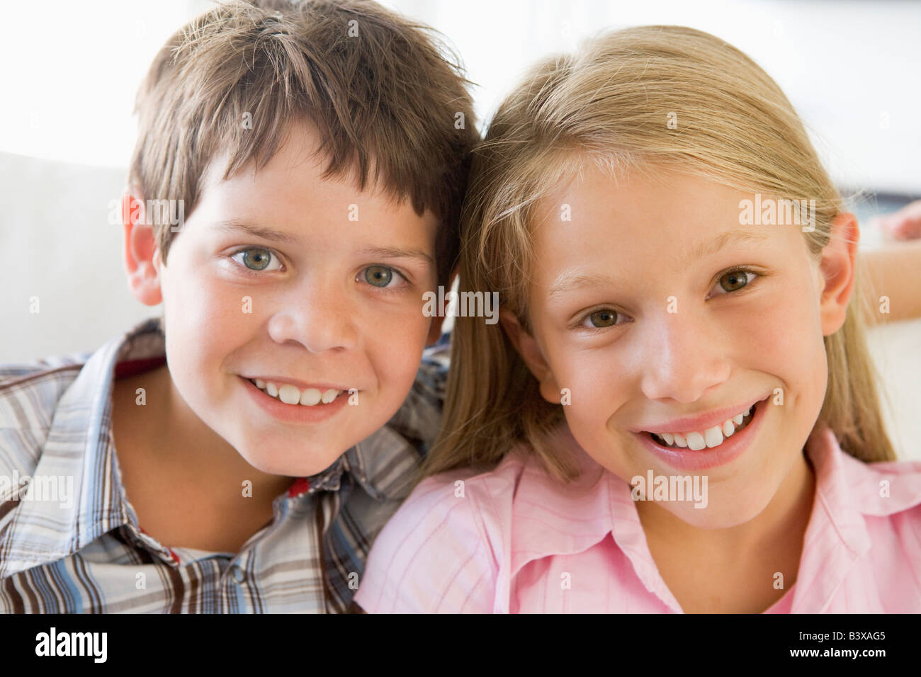 Brother And Sister Sitting Side By Side On A Couch Stock Photo
