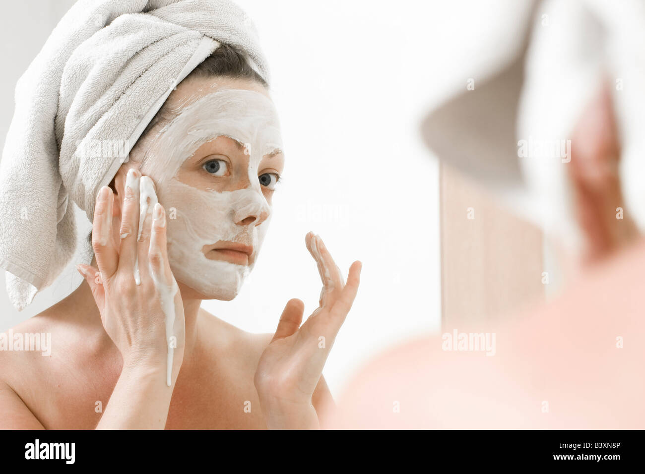 Young Woman applying a face mask whilst looking in a mirror Stock Photo