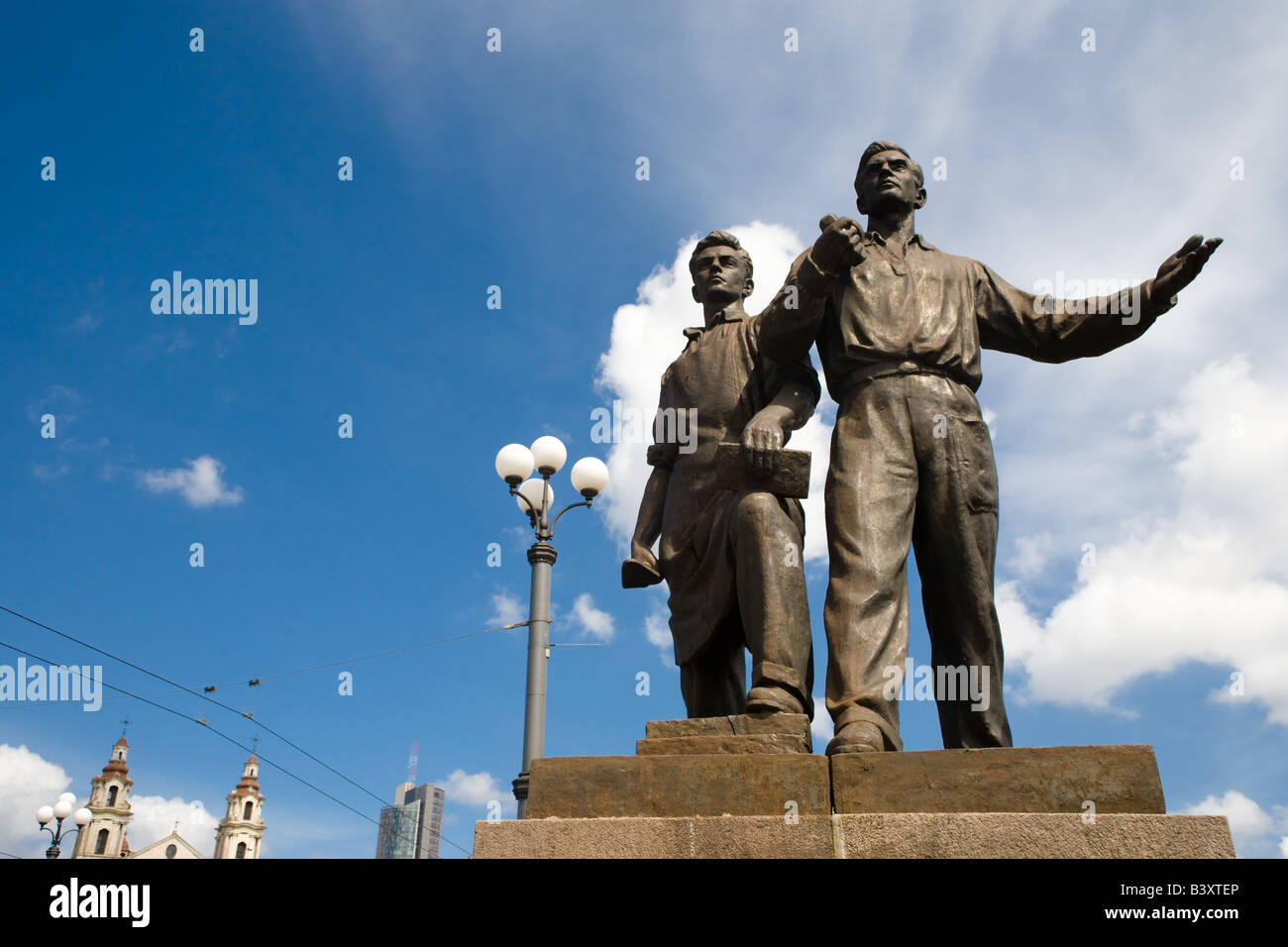 Two bronze Social Realism sculptures gesture boldly before buildings and a blue sky in Vilnius Lithuania on the Green Bridge. Stock Photo