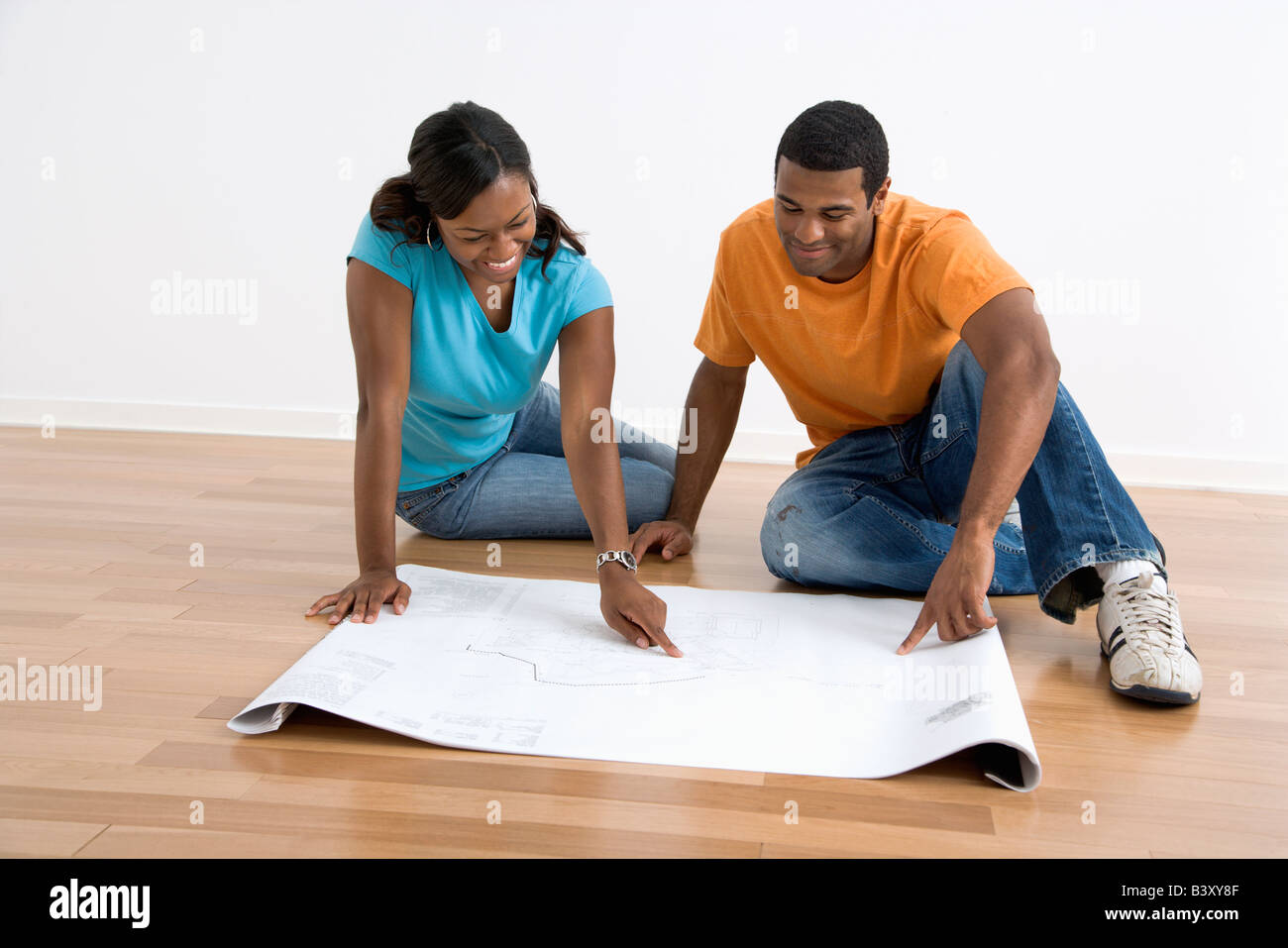 African American male and female couple sitting on floor looking at architectural blueprints Stock Photo