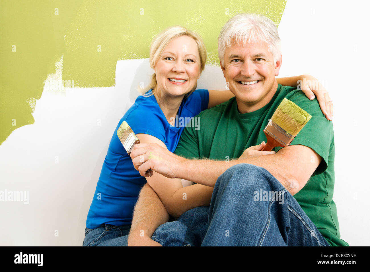 Middle aged couple snuggling in front of wall they are painting green Stock Photo