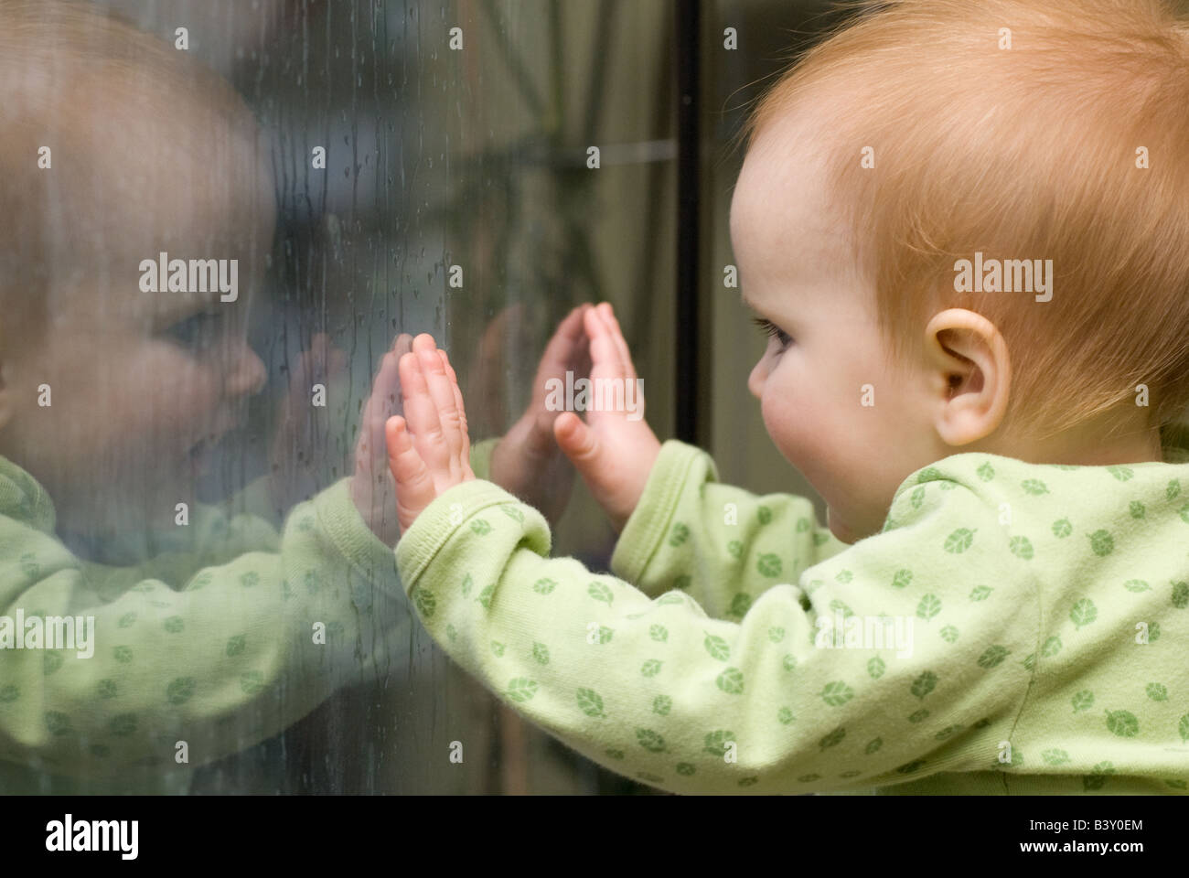 baby looking at her reflection on  window with raindrops Stock Photo
