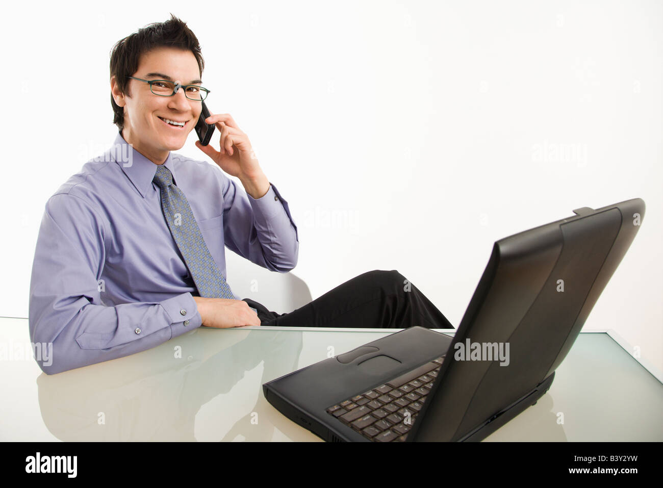 Smiling Asian businessman sitting at desk talking on cellphone Stock Photo