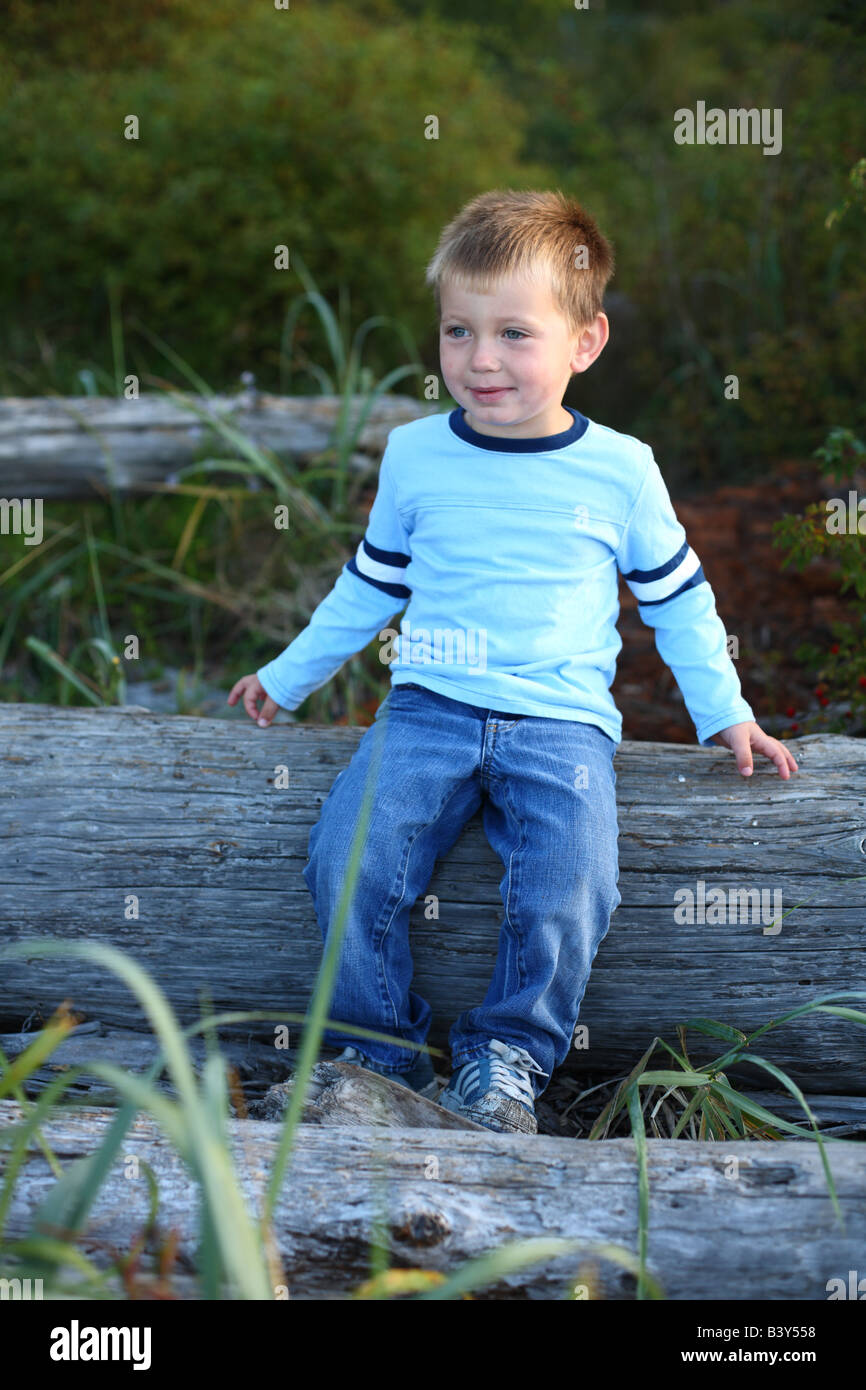 Young boy at beach sitting on drift wood Stock Photo