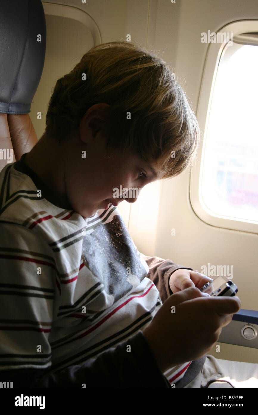 nine year old boy playing psp play station portable video game on airplane flight Stock Photo