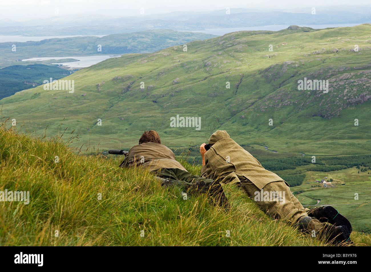 Scotland, Hebrides, Mull. As the riftle gets ready to take his shot a red deer stag, Benmore Estate stalker, Neilson Bissett, watches through binoculars. Stock Photo