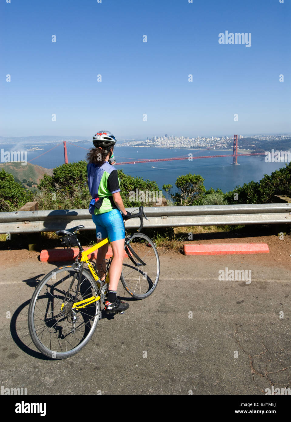 A woman bicyclist pauses at Hawk Hill in Marin County to admire the Golden Gate Bridge Stock Photo