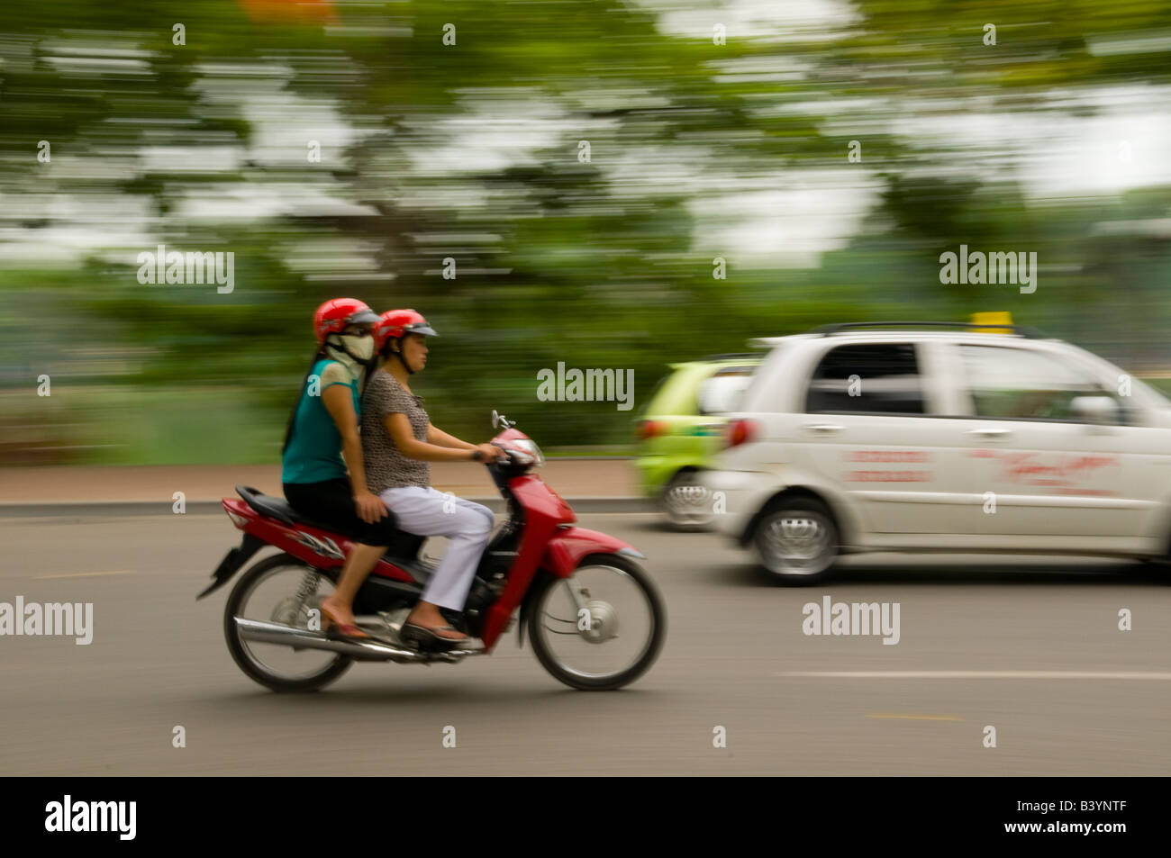 Two Vietnamese women on a motorbike in traffic Stock Photo