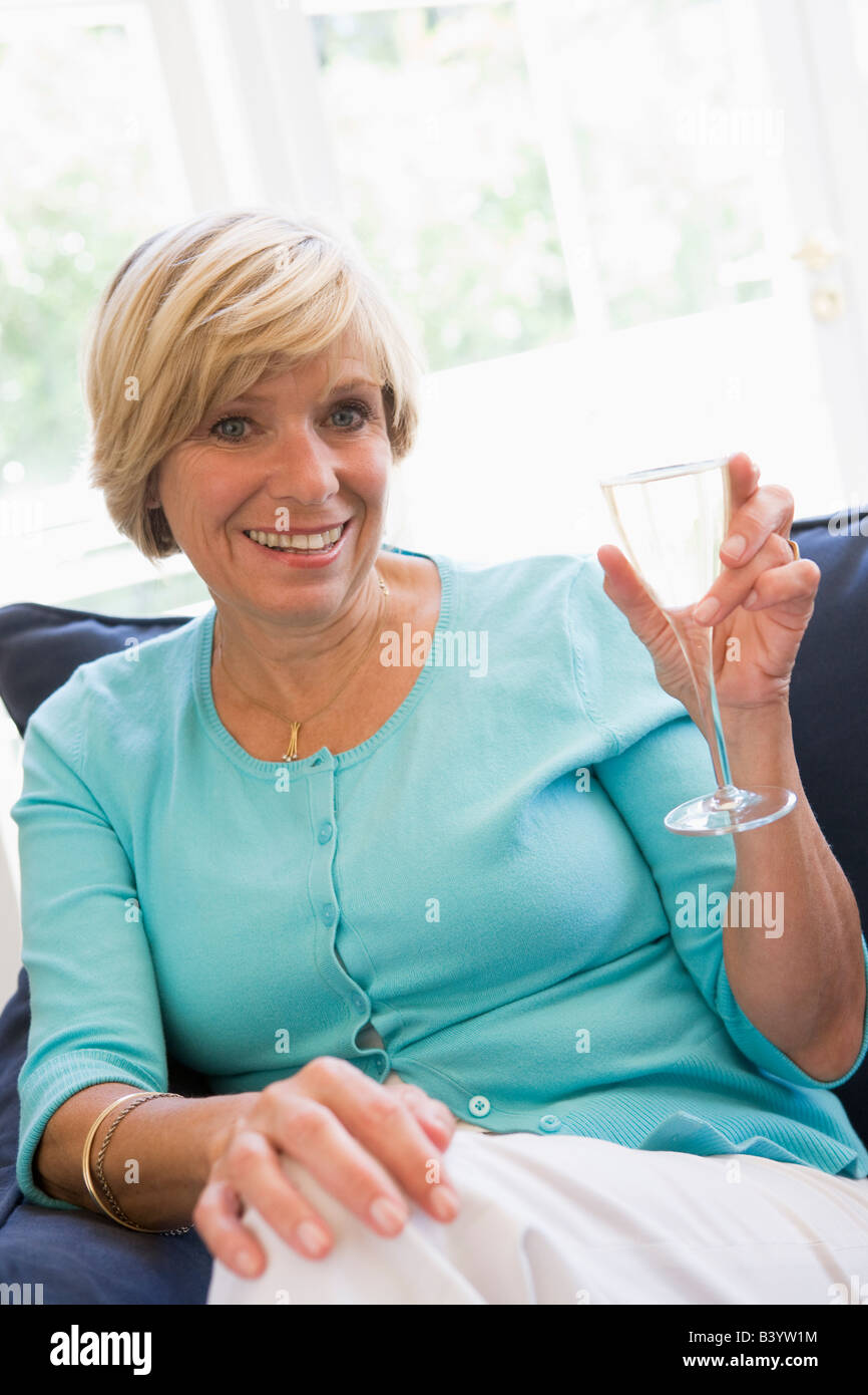 Woman sitting in living room with drink smiling Stock Photo - Alamy