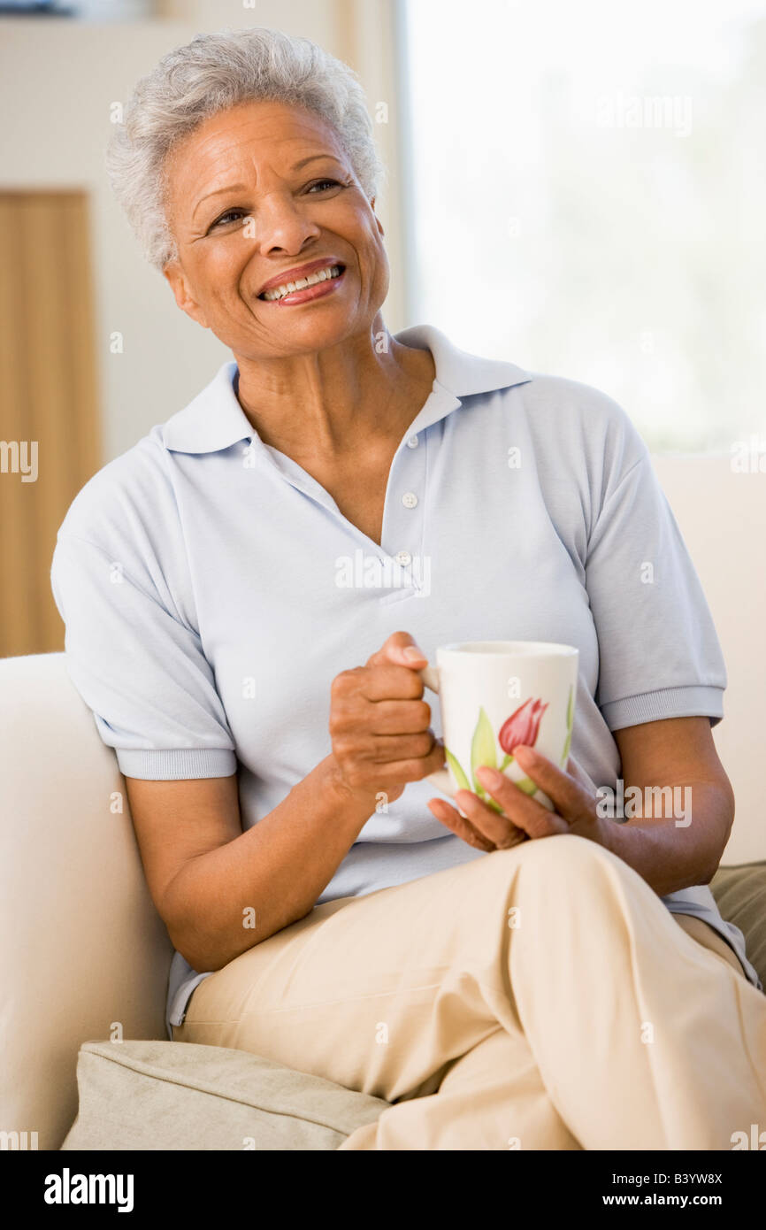 Woman sitting in living room with coffee smiling Stock Photo - Alamy